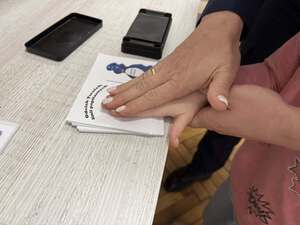 dłoń policjantki i dłoń dziecka podczas symbolicznych odcisków palcy na kartoniku