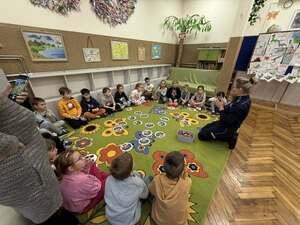 policjantka trzymająca krążek z obrazkiem i dzieci siedzące w kółku przed funkcjonariuszkom