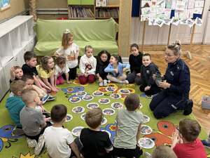 Policjantka siedząca przed dziećmi w kółeczku i w środku rozłożone memory