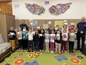 dzieci trzymające pieczątki z numerem alarmowym i stojący obok nich policjanci