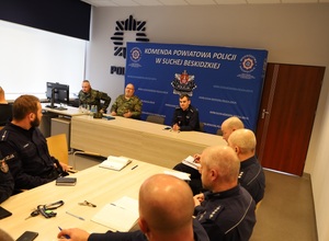 Zastępca komendanta powiatowego Policji w Suchej Beskidzkiej siedzący przy stole prezydialnym z przedstawicielami straży granicznej