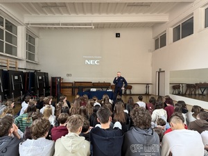 Hala sportowa wypełniona uczniami i stojacy przed uczniami policjnat