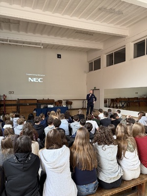 Duża grupa uczniów siedząca na materacach i słuchająca policjanta