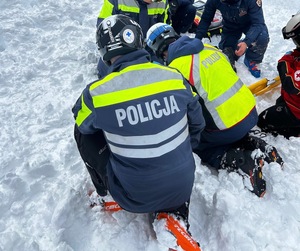 Umundurowani policjanci na nartach udzielają pomocy rannemu narciarzowi