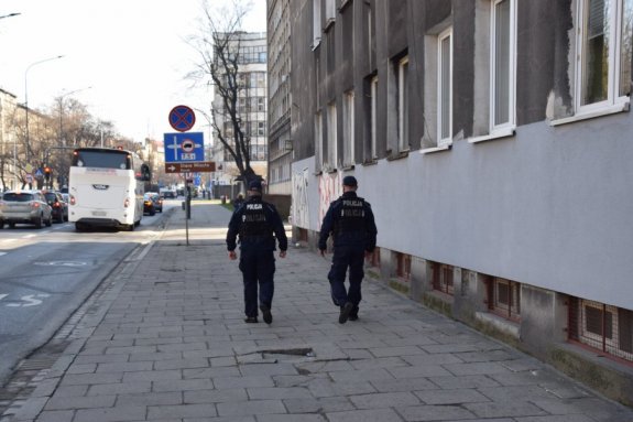 dwóch policjantów podczas patrolu idących chodnikiem wzdłuż kamienicy