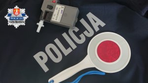 alcosensor wraz z tarczą do zatrzymywania samochodów na tle napisu policja wraz z logo KPP Sucha Beskidzka po lewej górnej stronie zdjęcia