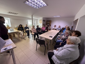 seniorzy siedzący na sali słuchający wykładu pana z bezpieczeństwa banku