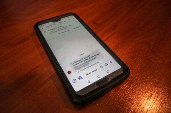 telefon komórkowy który wyświetla smsa z treścią &amp;quot;twoja paczka została zatrzymana przez służbę celną&amp;quot;