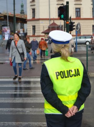 policjantka stojąca tyłem do zdjęcia na przeciwko przejścia dla pieszych na którym przechodzą ludzie