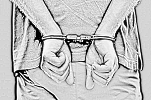 zdjęcie wykonane w kolorach czarno białych przestawiające kajdanki założone na ręce mężczyzny trzymane z tyłu