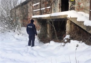 policjant stojący na śniegu przed opuszczonym budynkiem