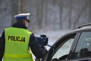 Umundurowany policjant wskazuje wynik pomiaru na urządzeniu laserowym mierzącym prędkość pojazdów.