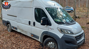 biały bus zakopany w gruncie na terenie lasu i stojący za nim radiowóz