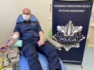 policjant oddający krew obok którego baner KPP Sucha Beskidzka