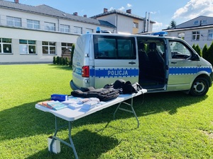 stoisko profilaktyczne wraz z policyjnym furgonem na tle szkoły w czasie słonecznej pogody