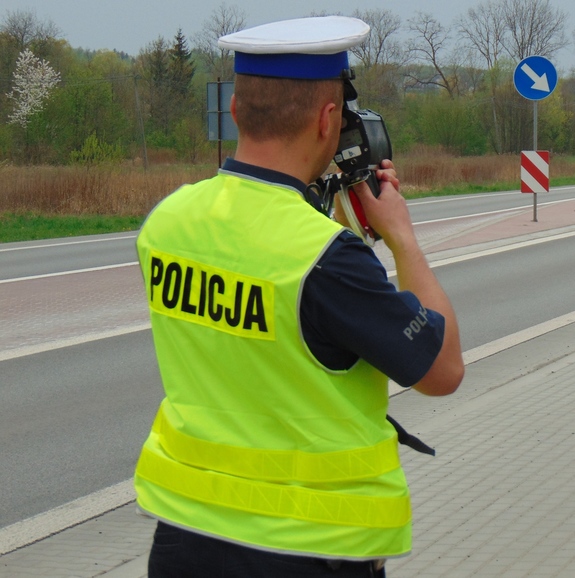 policjant ruchu drogowego mierzy miernikiem prędkość jadącego pojazdu