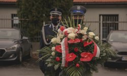 Zdjęcie przedstawiające policjanta trzymającego w rękach duży bukiet z kwiatami na tle którego stoi Komendant Wojewódzki Policji w Krakowie