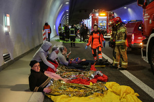 poszkodowani przykryci kocami termicznymi na jezdni i stojąca obok ratowniczka wraz ze strażakami