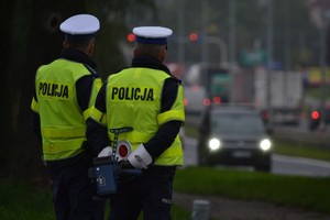 dwóch policjantów patrzących w stronę jadących samochodów