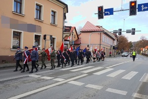 idący w stronę pomnika pochód na skrzyżowaniu na rynku w suchej beskidzkiej na czele którego idzie poczet suskich policjantów