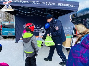 policjant przy stoisku uzupełnia w ulotki odblaskowy worek z logo kręci mnie bezpieczeństwo na stoku