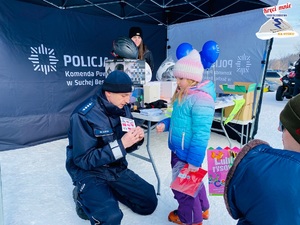 policjant  opowiada stojącej przed nim małej dziewczynce o numerach alarmowych zapisanych na kolorowej na karteczce