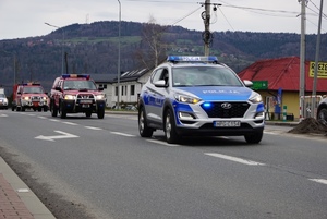 jadący policyjny radiowóz prowadzący kolumnę pojazdów straży biorących udział w ćwiczeniach