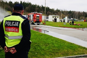 stojący tyłem dowódca Policji spoglądający na ćwiczących strażaków