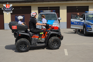 strażacki quad którego prowadzi strażak wiozący na placu komendy dziecko