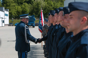 Pan Komendant Wojewódzki Policji ściskający dłoń jednemu z nowo przyjętych policjantów stojących na placu podczas ślubowania