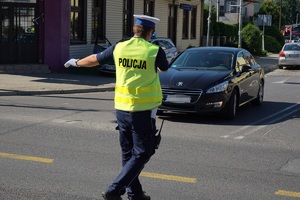policjant ruchu drogowego w białych rękawiczkach kierujący ruchem i przepuszczający czarny samochód