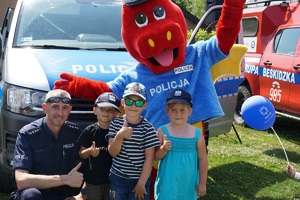 policjant wraz maskotką smokiem polickiem pozują do zdjęcia z dziećmi na tle policyjnego radiowozu