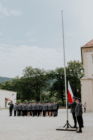 sztandar wciągany na maszt na tle policjantów śpiewający głośno Hymn Polski