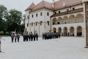 poczet sztandarowy i policjanci stojący w szeregach a w tle piękny suski zamek