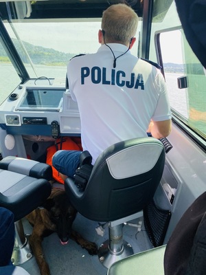 policjant na motorówce i leżący obok niego pies