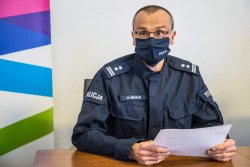 Umundurowany Przedstawiciel Komendy Wojewódzkiej Policji w Krakowie siedzący przy stole i trzymający kartkę papieru