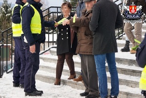 policjanci wręczający odblaski kobiecie i mężczyźnie wychodzący z kościoła