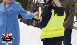 policjantka wręcza  kobiecie w niebieskim płaszczu opaskę odblaskową