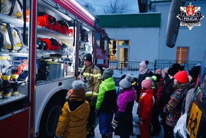 dzieci stojące w kolejce słuchające strażaka który prezentuje im sprzęt specjalistyczny